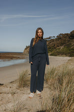 Load image into Gallery viewer, Woman in navy outfit standing on a beach with grass and ocean in the background